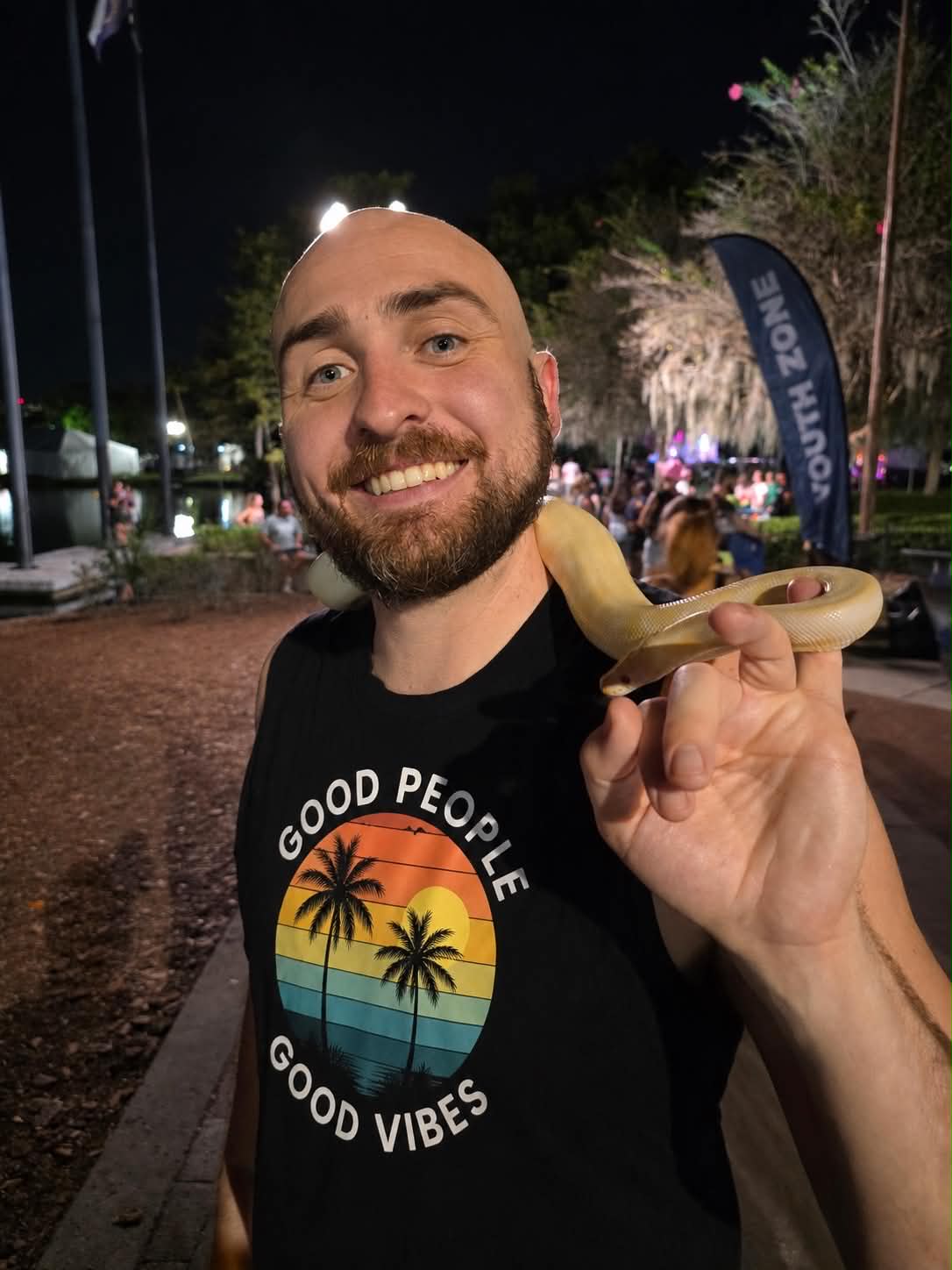 Patrick Hutchison smiling while holding a light-colored snake outdoors